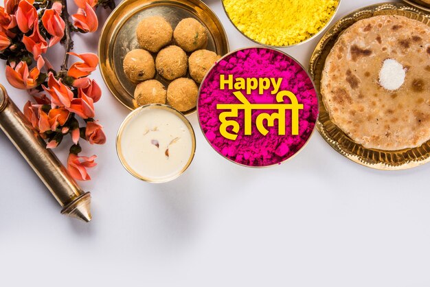 Carte de voeux Happy Holi conçue montrant des aliments traditionnels indiens sucrés et salés, des fleurs et des couleurs en poudre disposées sur fond blanc ou argile. Mise au point sélective