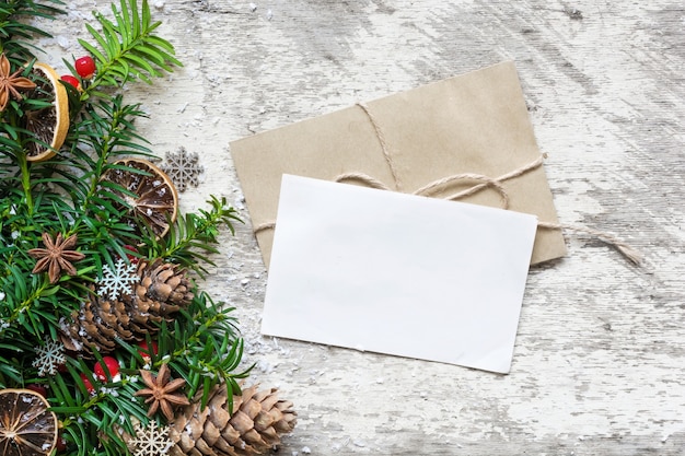 Photo carte de voeux de noël blanc vierge et enveloppe avec branches de sapin, décorations alimentaires et pommes de pin