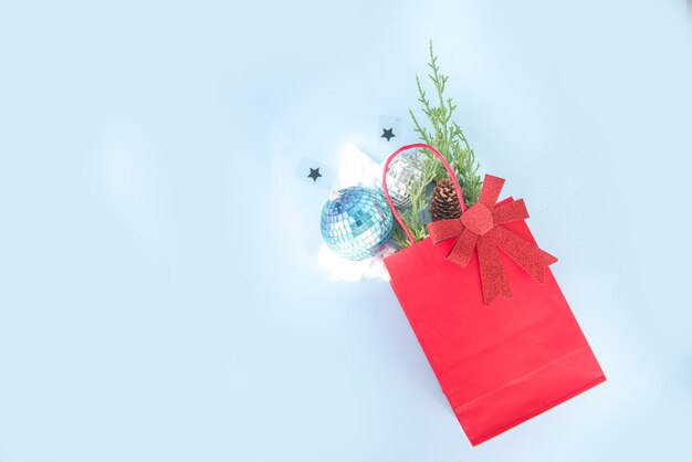 Carte de voeux de Noël simple, invitation à une fête, vente flatlay abstraite avec boules de Noël disco, branches de sapin, sac en papier avec noeud festif, sur fond bleu clair vue de dessus de l'espace de copie