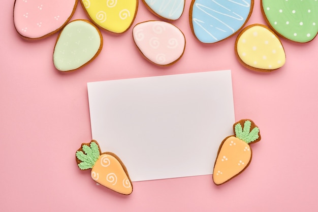 Carte de voeux de Pâques avec des lapins colorés, des œufs, des poulets et des carottes biscuits en pain d'épice sur fond rose avec espace de copie. Vue de dessus.