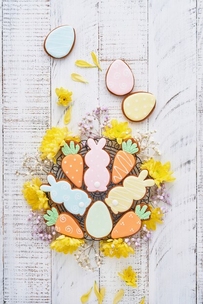 Carte de voeux de Pâques avec des lapins colorés, des œufs, des poulets et des carottes biscuits en pain d'épice sur fond vieux en bois blanc avec espace de copie. Vue de dessus.