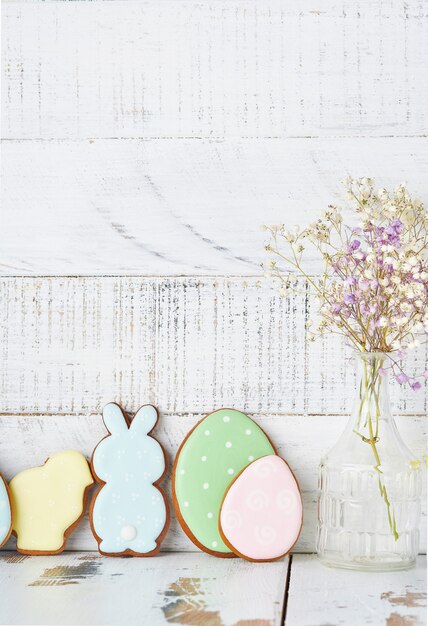 Carte de voeux de Pâques avec des lapins colorés, des oeufs, des poulets et des carottes biscuits en pain d'épice sur fond vieux en bois blanc avec espace de copie. Vue de dessus.