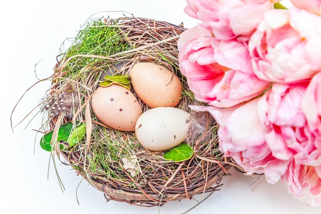 Carte de voeux de printemps. Oeufs de Pâques en nid et bouquet de fleurs de tulipes fraîches roses sur fond de bois blanc rustique