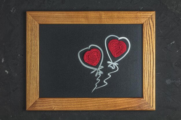 Photo carte de voeux saint valentin avec coeur au crochet en laine rouge sur une surface noire dans un cadre en bois vue de dessus plat copie espace