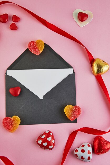 Carte de voeux de la Saint-Valentin avec des coeurs de bonbons et un ruban rouge sur fond rose.