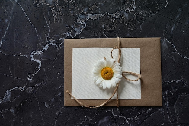 Une carte de voeux vide avec une enveloppe brune et une fleur blanche pour maman sur une table en bois de style vintage et avec des vignettes