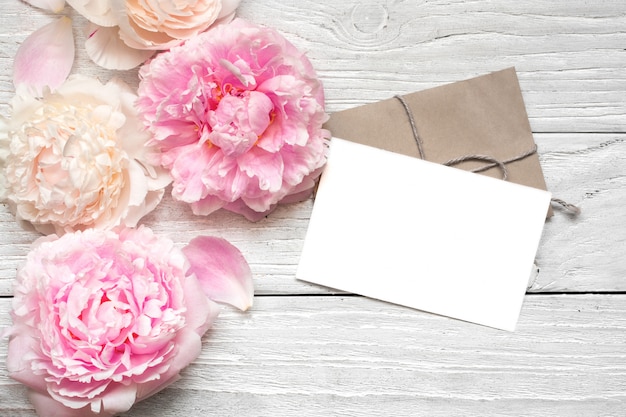 Carte de voeux vierge ou invitation de mariage avec des fleurs de pivoine roses et crémeuses sur une table en bois blanche.