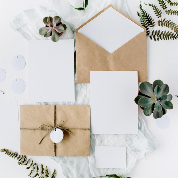 Cartes d'invitation de mariage, enveloppes d'artisanat, roses roses et rouges et feuilles vertes sur blanc