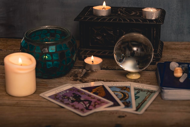 Des cartes de tarot dont Le Fou et Les Amoureux aux côtés de cristaux et de bougies sur une table en bois texturée