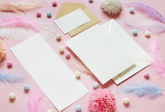 Cartes vierges et enveloppe près de fleurs pastel pompons et plumes près de l'anneau dans une boîte cadeau sur rose