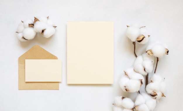 Cartes vierges et enveloppe avec vue de dessus de fleurs de coton sur la maquette de mariage blanc