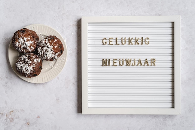 Photo un carton blanc avec le texte en lettres dorées orthographiant gelukkig nieuwjaar néerlandais pour bonne année avec oliebollen à côté