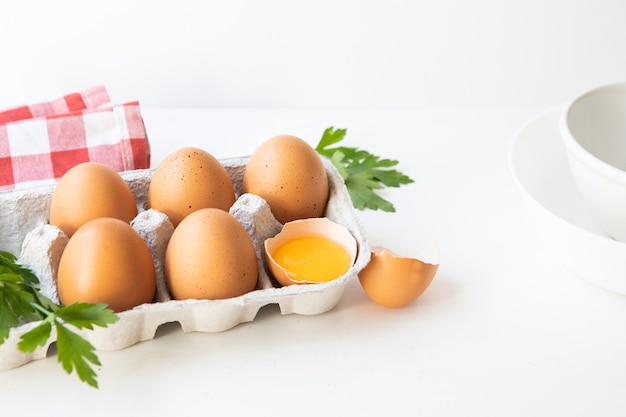 Carton d'oeufs sur table blanche, persil et torchon avec capsule blanche