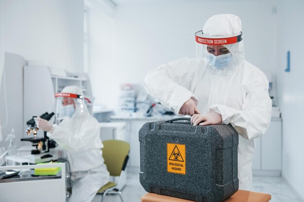 Photo avec un cas de danger biologique des travailleuses médicales en uniforme de protection travaillent sur le vaccin covid19