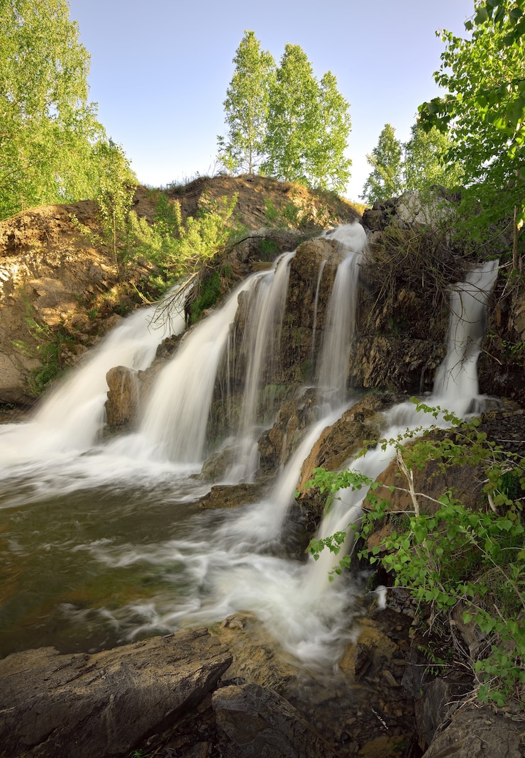 Cascade de Belovsky au printemps Une petite cascade parmi les rochers entourée de bouleaux