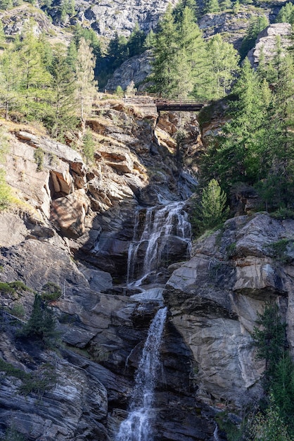 Photo la cascade du tripletier lillaz avec sentier et pont chancelant vue depuis le bas de la vallée de cogne aosta