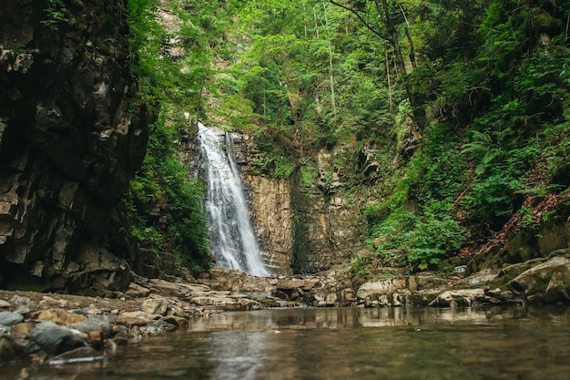 Cascade avec un lac parmi les rochers et la forêt.