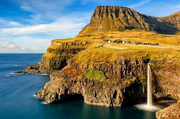 cascade Mulafossur et l'océan Atlantique Nord. Village de Gasadalur sous de légers nuages et ciel bleu. Île de Vagar. Îles Féroé