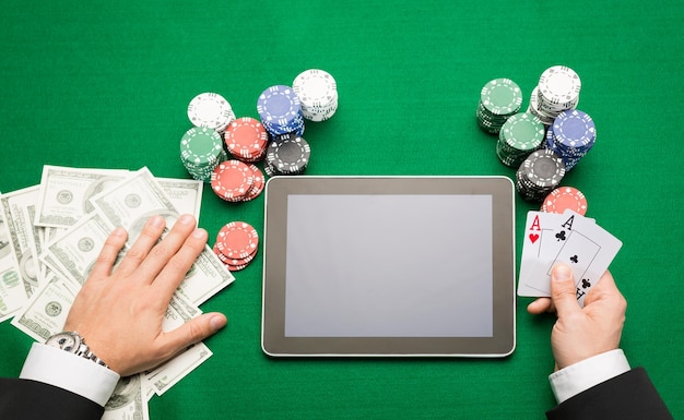 casino, jeu en ligne, technologie et concept humain - gros plan sur un joueur de poker avec des cartes à jouer, un ordinateur tablette et des jetons à la table de casino verte