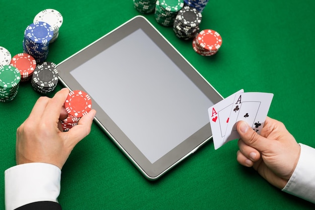 casino, jeu en ligne, technologie et concept humain - gros plan sur un joueur de poker avec des cartes à jouer, un ordinateur tablette et des jetons à la table de casino verte