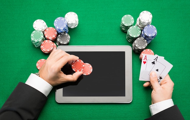 casino, jeu en ligne, technologie et concept humain - gros plan sur un joueur de poker avec des cartes à jouer, un ordinateur tablette et des jetons à la table de casino verte