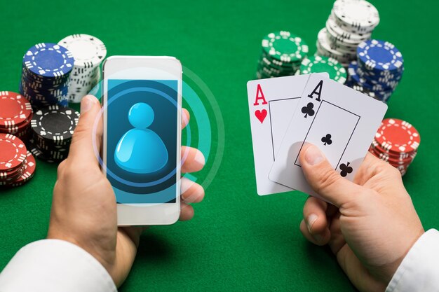 casino, jeu en ligne, technologie et concept humain - gros plan sur un joueur de poker avec des cartes à jouer, un smartphone et des jetons à la table de casino verte