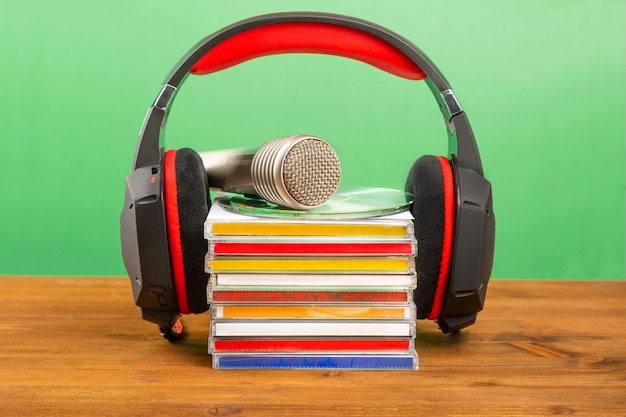 Casque avec CD et un microphone audio sur une table en bois, sur un mur végétal.