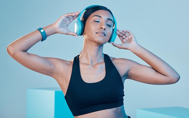 Casque de fitness et femme isolée sur fond bleu pour l'entraînement ou l'exercice de la musique Gen z sports et personne biraciale écoutant sur la technologie audio santé mentale ou bien-être en studio