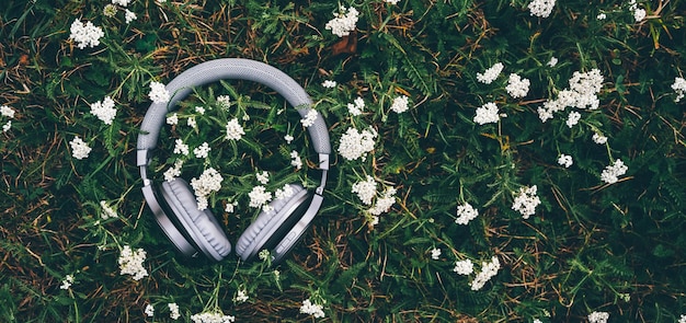 Le casque sur l'herbe avec des fleurs blanches Technologie quotidienne et concept d'été Longue bannière avec espace de copie