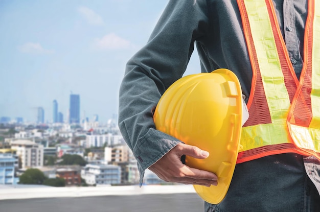 Le casque jaune est entre les mains d'un ouvrier du bâtiment avec un arrière-plan de construction de ville