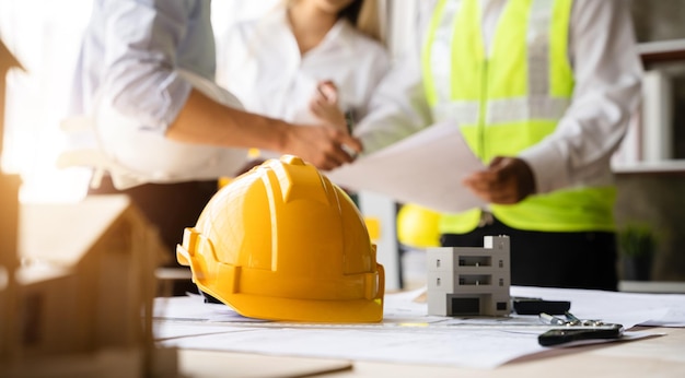 Casque jaune sur l'établi avec des équipes d'ingénieurs travaillant ensemble portant des casques de travail sur le chantier de construction Équipe professionnelle de l'industrie asiatique