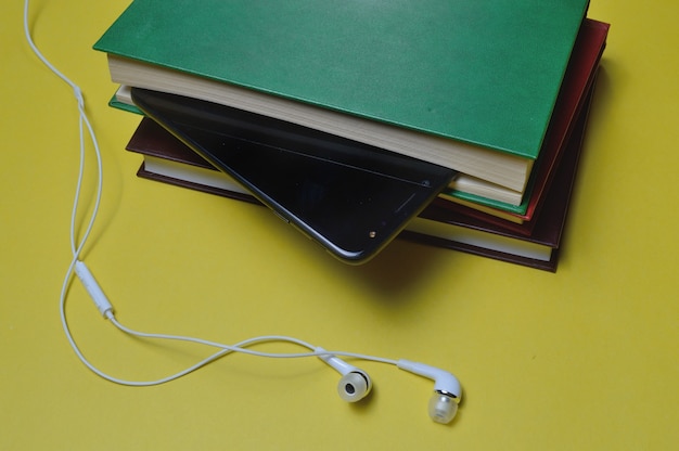 Casque avec des livres et un smartphone sur fond jaune.