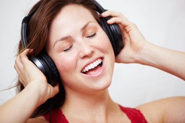 Casque de musique et chant par une femme heureuse en studio avec piste audio ou chanson sur fond blanc Visage d'écouteurs et personne de sexe féminin diffusant une radio de podcast ou une liste de lecture en ligne et un abonnement