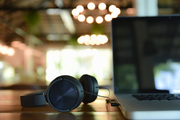 Casque noir et ordinateur portable sur la table en bois sur le café flou. Thème de création musicale numérique.