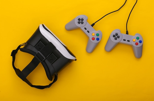 Casque de réalité virtuelle, manettes de jeu rétro sur fond jaune. Divertissement, jeu vidéo 3d. Vue de dessus