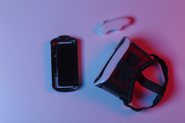 Casque de réalité virtuelle, smartphone et joystick en néon dégradé bleu rouge. Vue de dessus