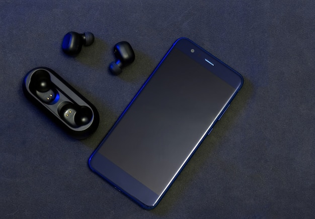 Casque sans fil noir avec téléphone portable bleu sur fond sombre.