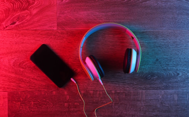 Casque et smartphone sur un plancher en bois avec une lueur dégradé rouge-bleu néon