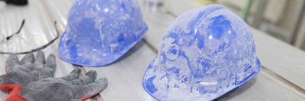 Casques de construction bleus poussiéreux sur une table blanche sécurité de rapprochement dans la construction protectrice
