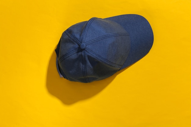 Casquette bleu jeans sur fond clair jaune avec une ombre profonde.