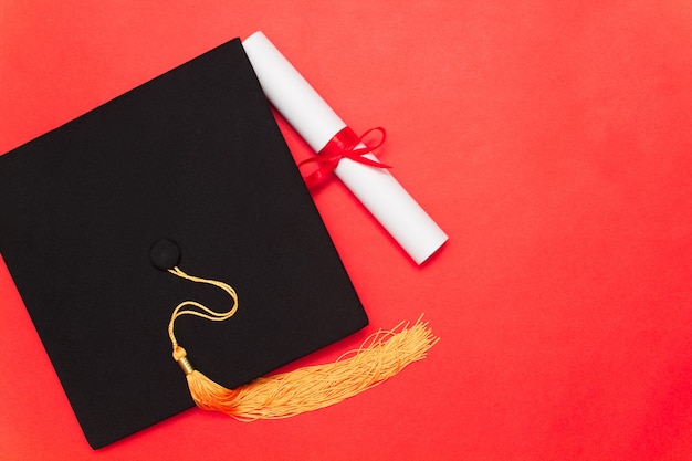 Casquette diplômée et diplôme avec ruban rouge sur fond rouge. Espace de copie