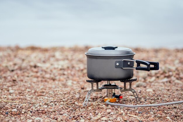 La casserole avec la bouillie se dresse sur le brûleur à gaz Réchaud de camping Sur le fond de la rivière