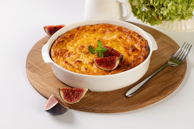 Casserole de caillé à la citrouille de forme ronde et blanche sur une planche en bois, une table blanche décorée de figues, un restaurant servant