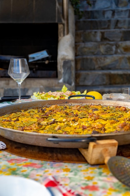 Une casserole de paella est posée sur une table avec un verre de vin et une nappe avec une nappe.