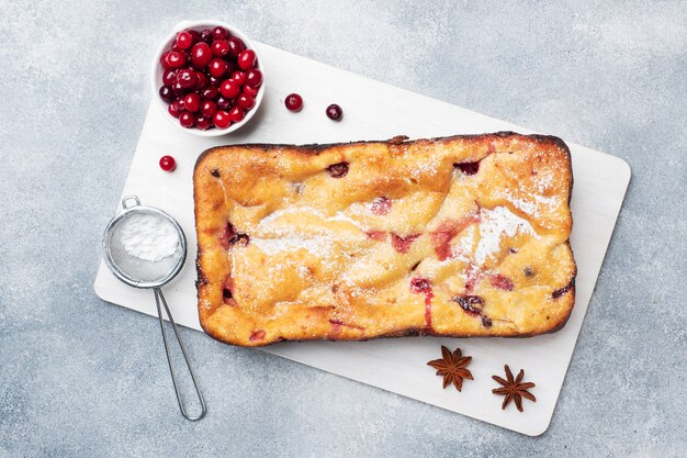 Photo casserole de tarte au fromage cottage avec des canneberges et des épices saupoudrées de sucre en poudre sur un support en bois. table en béton gris.