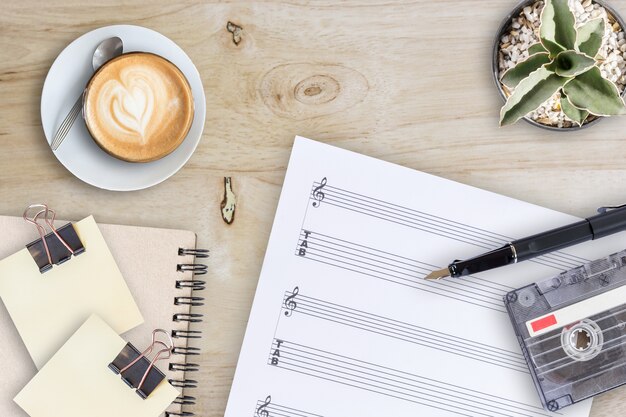 Cassette de cassette de plume de feuille de musique et café latte sur la table en bois