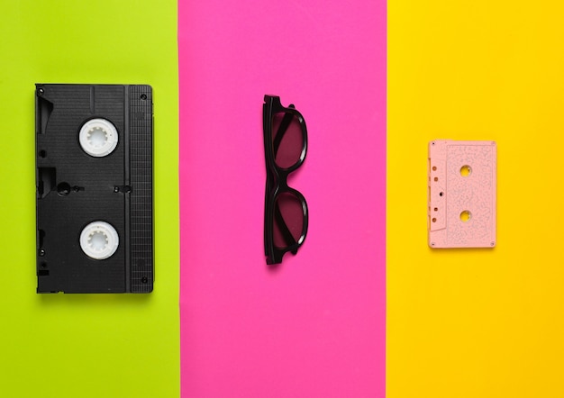 Cassette vidéo, lunettes de soleil, cassette audio sur une surface en papier multicolore. Tendance minimaliste, mise à plat, vue de dessus.