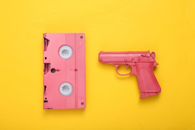 Cassette vidéo rose et pistolet sur fond jaune Mise en page créative Minimalisme Mise à plat Vue de dessus