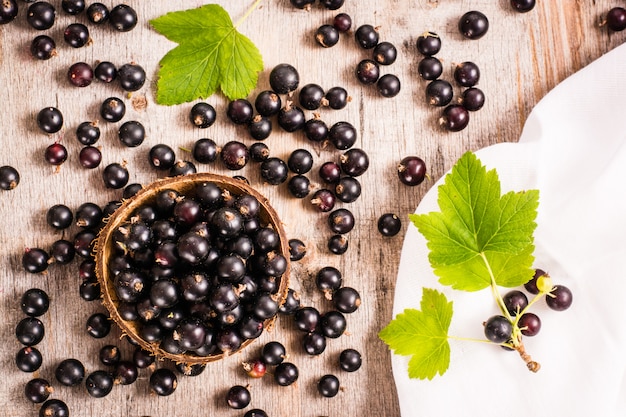 Cassis frais dans le bol. Beaucoup de groseilles et de feuilles éparpillées sur la table minable. Vue de dessus