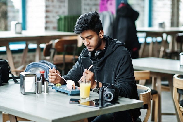 Casual et élégant jeune homme asiatique avec des écouteurs au café manger des sushis